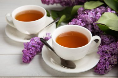 Bir fincan yeşil çay, arka planda bir demet leylağın üzerine serpiştirilmiş gri bir arkaplan. Kitaplar ve mumlarla romantik kompozisyon. Bahar çayı içeceği. Kopyalanacak yer.