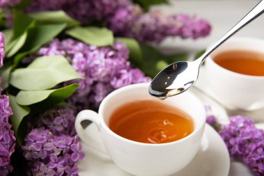 Bir fincan yeşil çay, arka planda bir demet leylağın üzerine serpiştirilmiş gri bir arkaplan. Kitaplar ve mumlarla romantik kompozisyon. Bahar çayı içeceği. Kopyalanacak yer.