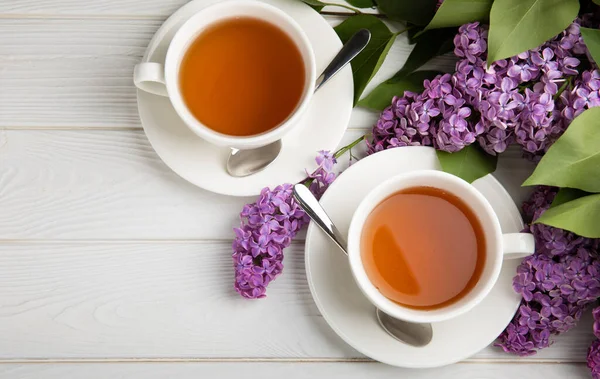 Bir fincan yeşil çay, arka planda bir demet leylağın üzerine serpiştirilmiş gri bir arkaplan. Kitaplar ve mumlarla romantik kompozisyon. Bahar çayı içeceği. Kopyalanacak yer.