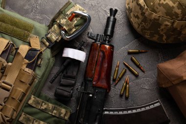 Askeri zırh, miğfer ve mühimmat, bir Kalaşnikof müfrezeli saldırı tüfeği ve ilk yardım turnikesi. Siyah bir mermer masanın üzerinde. Ordu kurşun geçirmez yelek. Düz yatıyordu. Askeri kavram.