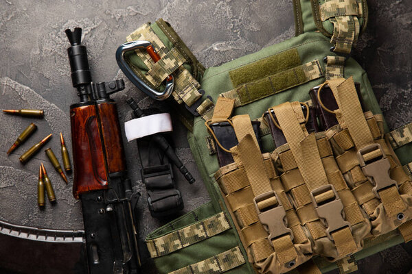 Military body armor, helmet and ammunition, a Kalashnikov assault rifle with matrons and a first aid tourniquet. On a black marble table. Army bulletproof vest. Flat lay. Military concept.