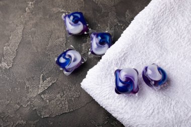 Siyah mermer arka planda çamaşır kapsülleri ve kar beyazı bir havlu. Çamaşır makinesinde çamaşır yıkamak için deterjan. Saflık kavramı. Metin için yer.