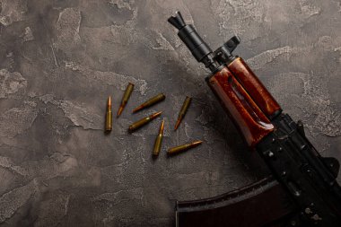 Siyah desenli mermer üzerine Kolashnikov saldırı tüfeği içeren mermiler ve cephane şarjörü. Metinde yer alan kompozisyon. Tahta arka planda tüfek ve kartuş. Askeri kavram.