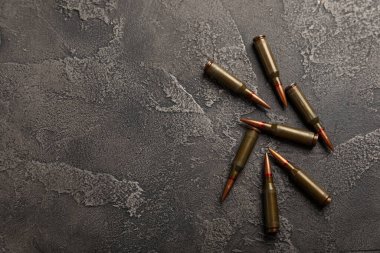 Siyah desenli mermer üzerinde mermiler. Kolashnikov saldırı tüfeğinin mermileri. Kısa mesafeden ateş edilmiş. Tüfek için fişekler ve tahta arka planda bir tüfek. Askeri bir kavram. Boşluğu kopyala