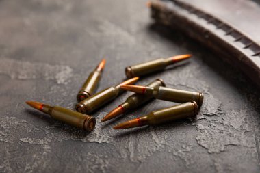 Siyah desenli mermer üzerinde mermiler. Kolashnikov saldırı tüfeğinin mermileri. Kısa mesafeden ateş edilmiş. Tüfek için fişekler ve tahta arka planda bir tüfek. Askeri bir kavram. Boşluğu kopyala