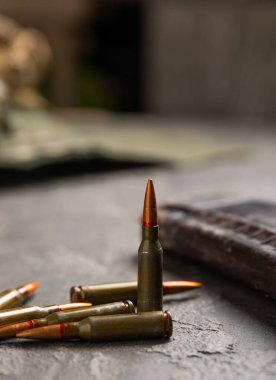 Siyah desenli mermer üzerinde mermiler. Kolashnikov saldırı tüfeğinin mermileri. Kısa mesafeden ateş edilmiş. Tüfek için fişekler ve tahta arka planda bir tüfek. Askeri bir kavram. Boşluğu kopyala