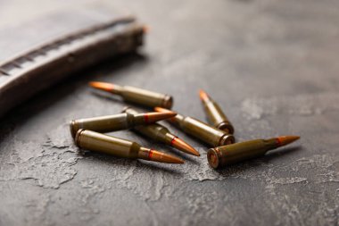Siyah desenli mermer üzerinde mermiler. Kolashnikov saldırı tüfeğinin mermileri. Kısa mesafeden ateş edilmiş. Tüfek için fişekler ve tahta arka planda bir tüfek. Askeri bir kavram. Boşluğu kopyala