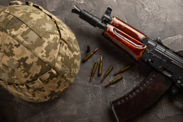 Bullets and ammo magazine with Kalashnikov assault rifle and hard hat on black textured marble. Composition with place for text. Cartridges for a rifle and a carbine on a wooden background. Military concept.