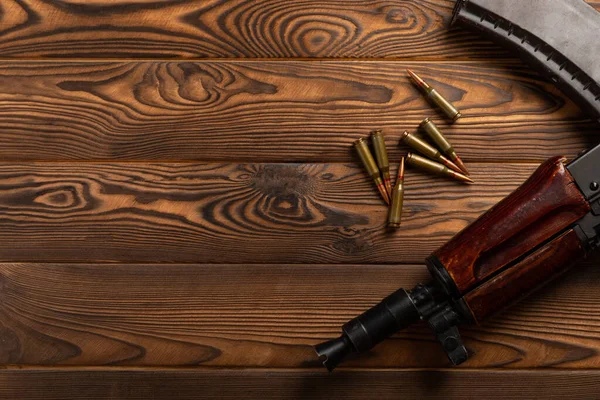 Bullets and ammo magazine with Kalashnikov assault rifle on brown wood. Composition with place for text. Cartridges for a rifle and a carbine on a wooden background. Military concept.