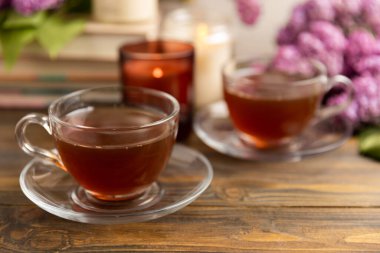 Kahverengi desenli ahşap bir demet leylağın arka planına karşı bir fincan yeşil çay. Kitaplar ve mumlarla romantik kompozisyon. Bahar çayı içeceği. Kopyalanacak yer. Romantik konsept.