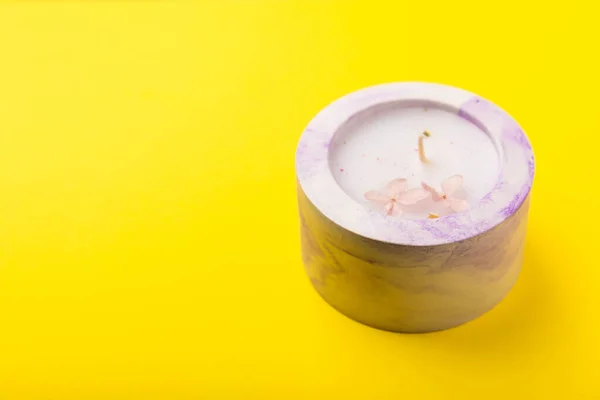 Candle in a lilac concrete candlestick on a bright yellow background.Lavender candle with dried flowers. Composition with eco-candles. Aromatherapy and relaxation.