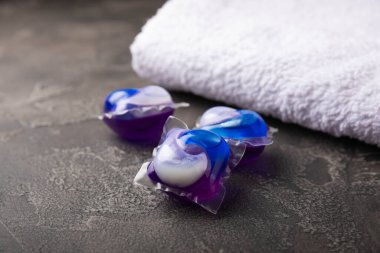 Siyah mermer arka planda çamaşır kapsülleri ve kar beyazı bir havlu. Çamaşır makinesinde çamaşır yıkamak için deterjan. Saflık kavramı. Metin için yer.