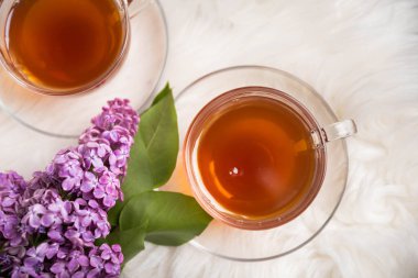 Bir demet leylağın arka planına karşı bir fincan yeşil çay. Kitaplar ve mumlarla romantik kompozisyon. Bahar çayı içeceği. Kopyalanacak yer. Romantik konsept.