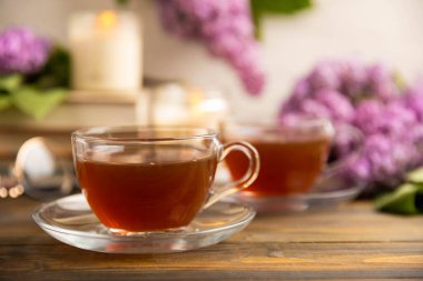 Bir demet leylağın arka planına karşı bir fincan yeşil çay. Kitaplar ve mumlarla romantik kompozisyon. Bahar çayı içeceği. Kopyalanacak yer. Romantik konsept.