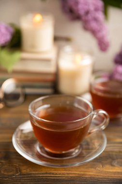 Bir demet leylağın arka planına karşı bir fincan yeşil çay. Kitaplar ve mumlarla romantik kompozisyon. Bahar çayı içeceği. Kopyalanacak yer. Romantik konsept.