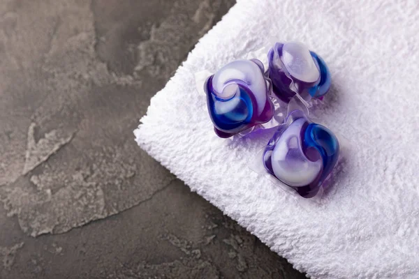 Siyah mermer arka planda çamaşır kapsülleri ve kar beyazı bir havlu. Çamaşır makinesinde çamaşır yıkamak için deterjan. Saflık kavramı. Metin için yer.