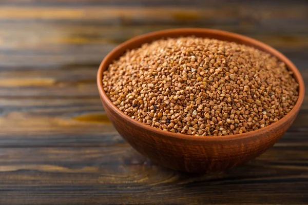 Kahverengi ahşap arka planda bir kasede karabuğday. Çiğ karabuğday. Glütensiz güveç için malzemeler. Sağlıklı yiyecekler. Kopyalanacak yer.
