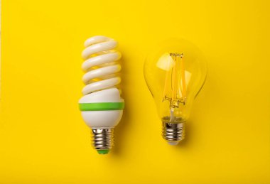 Elektrik ampulleri. Enerji verimliliği kavramı. LED lamba parlak lambaya karşı. Sarı arka planda kompozisyon. Ekonomik ve çevre dostu bir ampul kavramı kullan.