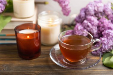 Bir demet leylağın arka planına karşı bir fincan yeşil çay. Kitaplar ve mumlarla romantik kompozisyon. Bahar çayı içeceği. Kopyalanacak yer. Romantik konsept.