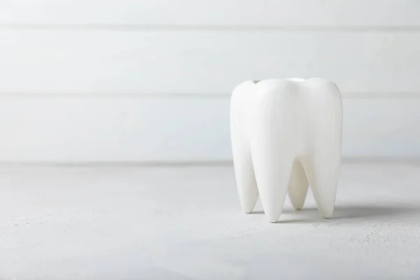 White tooth model on a white wooden background. The concept of dental hygiene. Prevention of plaque and gum disease.MOCKUP