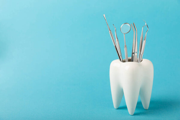 White healthy tooth and various dental tools for dental care.Dental concept.Composition on a blue background.Side view. Copy space.MOCKUP.Dental hygiene.