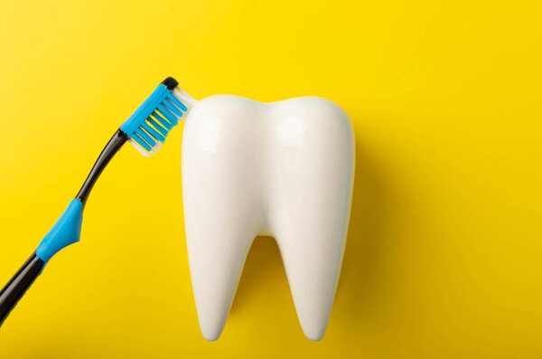 Cleaning model of a white tooth with a toothbrush on a yellow background. The concept of dental hygiene. Prevention of plaque and gum disease.MOCKUP