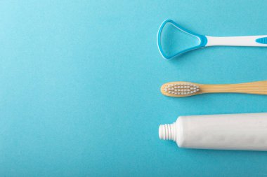 Bir tüp diş macunu, bir diş fırçası ve mavi arka planda bir dil temizleyici. Diş macununu tazeleyip beyazlatıyor. Ders için boşluk kopyala. Ciklet hastalıklarını ve bakterileri önle. düz yat