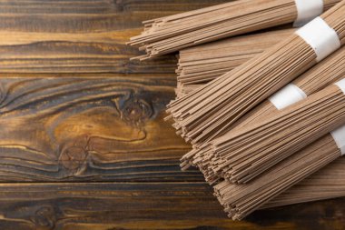 Kahverengi desenli ahşap arka planda karabuğday makarnası. Çiğ erişte. Glütensiz yemek için gerekli malzemeler. Kurutulmuş karabuğday sobalı erişte. Geleneksel Japon yemekleri. Sağlıklı yiyecekler. Kopyalanacak yer.