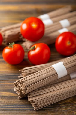 Kahverengi ahşap üzerinde kiraz domatesli karabuğday makarnası. Çiğ makarna. Glütensiz yemek için gerekli malzemeler. Sağlıklı yiyecekler. Kopyalanacak yer.