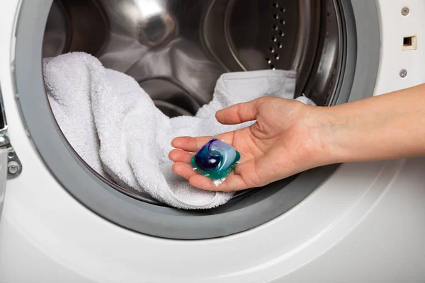 Woman putting laundry detergent capsule into washing machine indoors, closeup.Colorful laundry eco gel in capsule. Washing clothers.The concept of washing and cleanliness