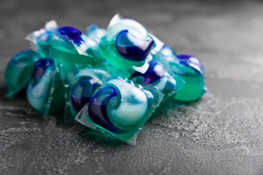 Koyu dokulu arka planda çamaşır kapsülleri. Çamaşır makineleri için sıvı çamaşır tozu içeren kapsüller. Yıkama ve temizlik kavramı. Boşluğu kopyala.