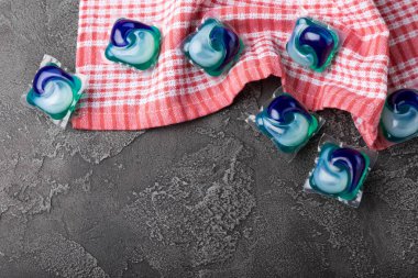 Karanlık desenli arka planda mutfak havlusu olan çamaşır kapsülleri. Çamaşır makineleri için sıvı çamaşır tozu içeren kapsüller. Yıkama ve temizlik kavramı. Boşluğu kopyala.