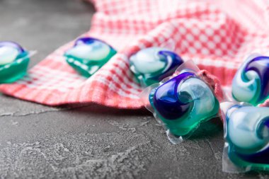 Karanlık desenli arka planda mutfak havlusu olan çamaşır kapsülleri. Çamaşır makineleri için sıvı çamaşır tozu içeren kapsüller. Yıkama ve temizlik kavramı. Boşluğu kopyala.