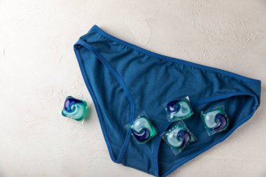 Açık renk arka planda çamaşır kapsülleri olan mavi kadın külotları. Çamaşır makinesi için sıvı deterjanı olan kapsüller. Yıkama ve temizlik konsepti. Boşluğu kopyala.