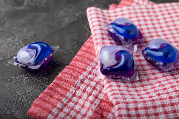 Karanlık desenli arka planda mutfak havlusu olan çamaşır kapsülleri. Çamaşır makineleri için sıvı çamaşır tozu içeren kapsüller. Yıkama ve temizlik kavramı. Boşluğu kopyala.