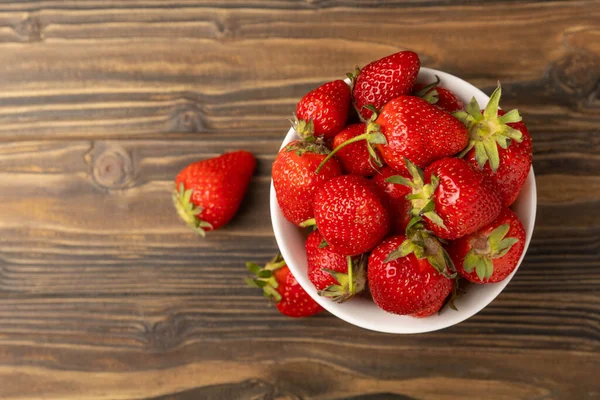 Kahverengi ahşap bir masanın üzerindeki kasede taze olgun sulu çilekler. Çilekli yaz kompozisyonu. Meyve konsepti. Vitamin. Eko meyveler. Boşluğu kopyala