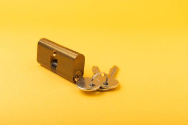 Sarı arka planda yeni kapı kilidi. Patent ve anahtarlar ön kapıdan. Silindir kilidinin iç mekanizması ve bir takım anahtarlarla temas kurun. Emlak kavramı