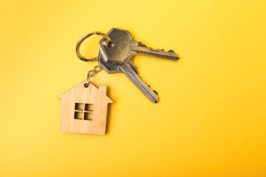 Evin anahtarlığı ev şeklinde. Sarı arka planda kompozisyon. Emlak ve sigorta konsepti. Kopya alanı..