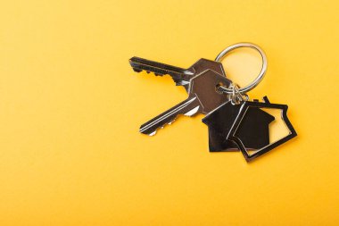 Evin anahtarlığı ev şeklinde. Sarı arka planda kompozisyon. Emlak ve sigorta konsepti. Kopya alanı..