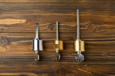 Kahverengi ahşap arka planda yeni bir kapı kilidi. Patent ve ön kapının anahtarları. Silindir kilidinin iç mekanizması ve bir takım anahtarlarla temas kurun. Emlak kavramı