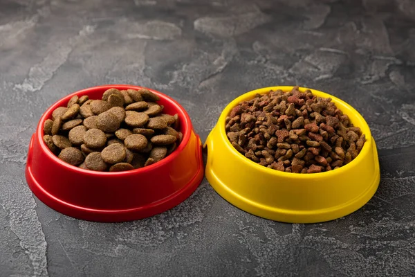 Dry food for cats and dogs in a yellow and red bowl on  cement background.Vitamins and nutrients for good health and pet energy.