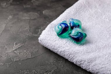 Siyah mermer arka planda çamaşır kapsülleri ve kar beyazı bir havlu. Çamaşır makinesinde çamaşır yıkamak için deterjan. Saflık kavramı. Metin için yer.