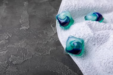 Siyah mermer arka planda çamaşır kapsülleri ve kar beyazı bir havlu. Çamaşır makinesinde çamaşır yıkamak için deterjan. Saflık kavramı. Metin için yer.