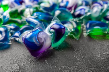 Koyu dokulu arka planda çamaşır kapsülleri. Çamaşır makineleri için sıvı çamaşır tozu içeren kapsüller. Yıkama ve temizlik kavramı. Boşluğu kopyala.