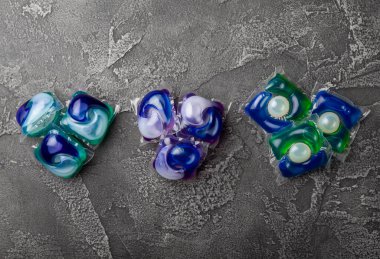 Koyu dokulu arka planda çamaşır kapsülleri. Çamaşır makineleri için sıvı çamaşır tozu içeren kapsüller. Yıkama ve temizlik kavramı. Boşluğu kopyala.