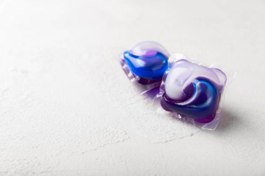 Çamaşır deterjanı yıkamak için kapsüller çamaşır makinesinde çamaşır yıkamak için kapsüller beyaz çimento arka planında. Temizlik kavramı. Çamaşır makinesi için sıvı deterjanlı kapsüller..