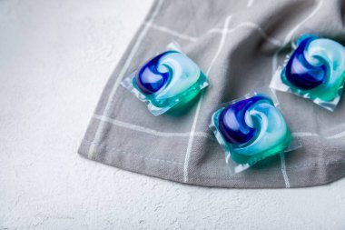 Çamaşır kapsülleri ve mutfak havlusu beyaz mermer arka planda. Çamaşır makinesinde çamaşır yıkamak için deterjan. Saflık kavramı. Metin için yer.