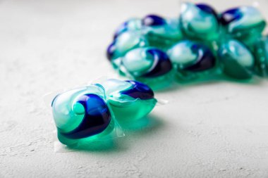 Çamaşır deterjanı yıkamak için kapsüller çamaşır makinesinde çamaşır yıkamak için kapsüller beyaz çimento arka planında. Temizlik kavramı. Çamaşır makinesi için sıvı deterjanlı kapsüller..