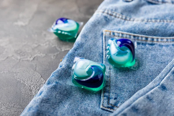 Laundry capsules with blue jeans on a black marble background. Laundry detergent for washing clothes in a washing machine. The concept of purity. Place for text.