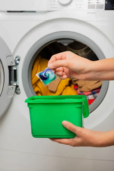 Woman putting laundry detergent capsule into washing machine indoors, closeup.Colorful laundry eco gel in capsule. Washing clothes.The concept of washing and cleanliness